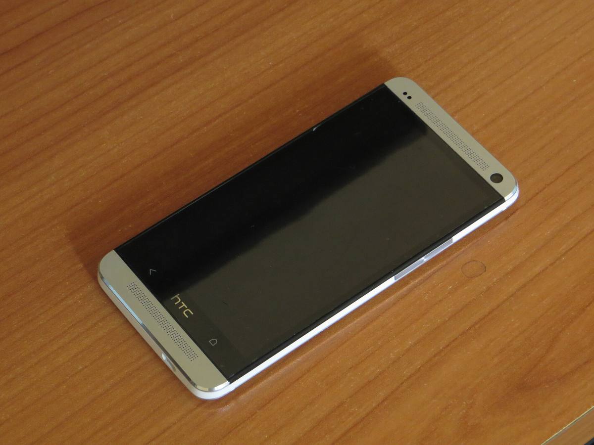 Stříbrný telefon HTC One leží displejem vzhůru na dřevěném stole